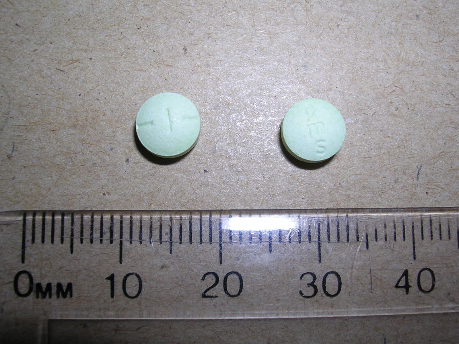 Two small pale-green hydromorphone tablets next to a millimetre ruler