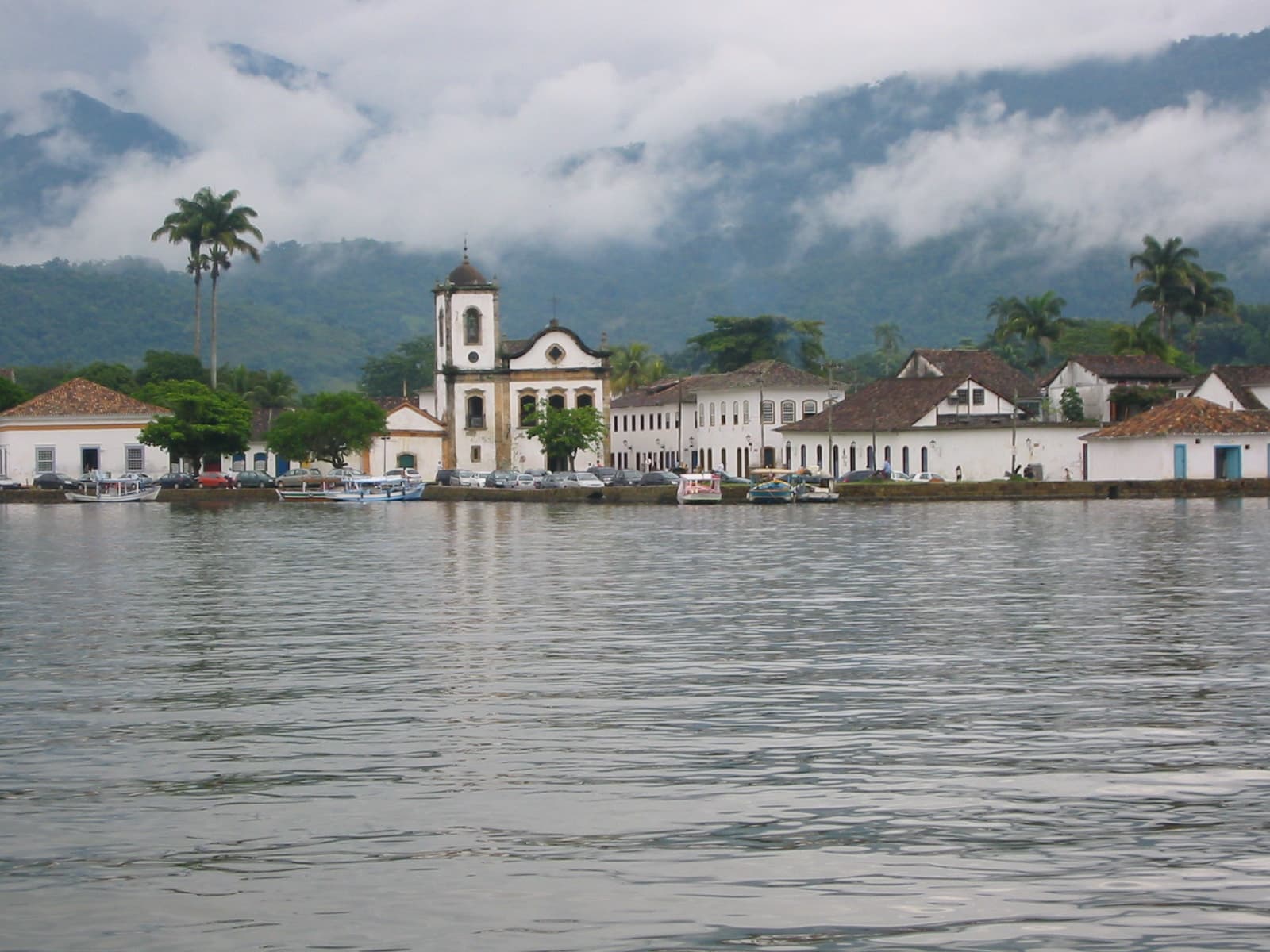 The historic waterfront of Paraty seen from calm water, mist on the mountains behind