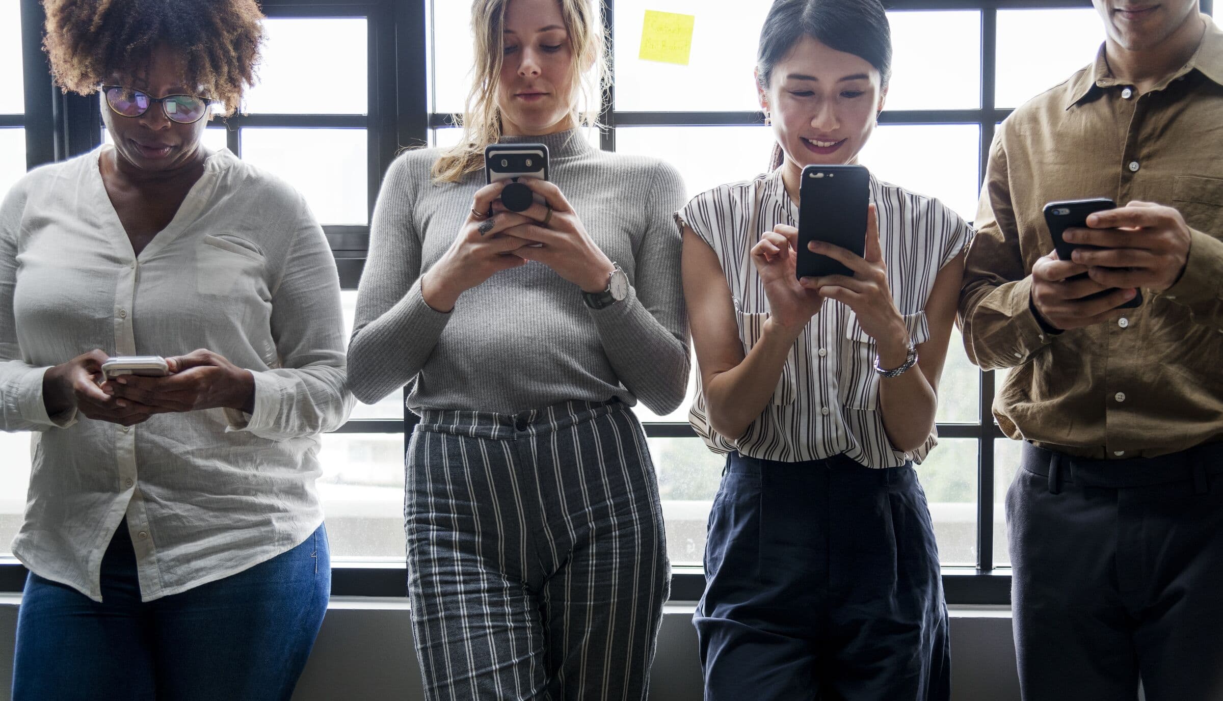 Four people in a row, each looking down at a phone