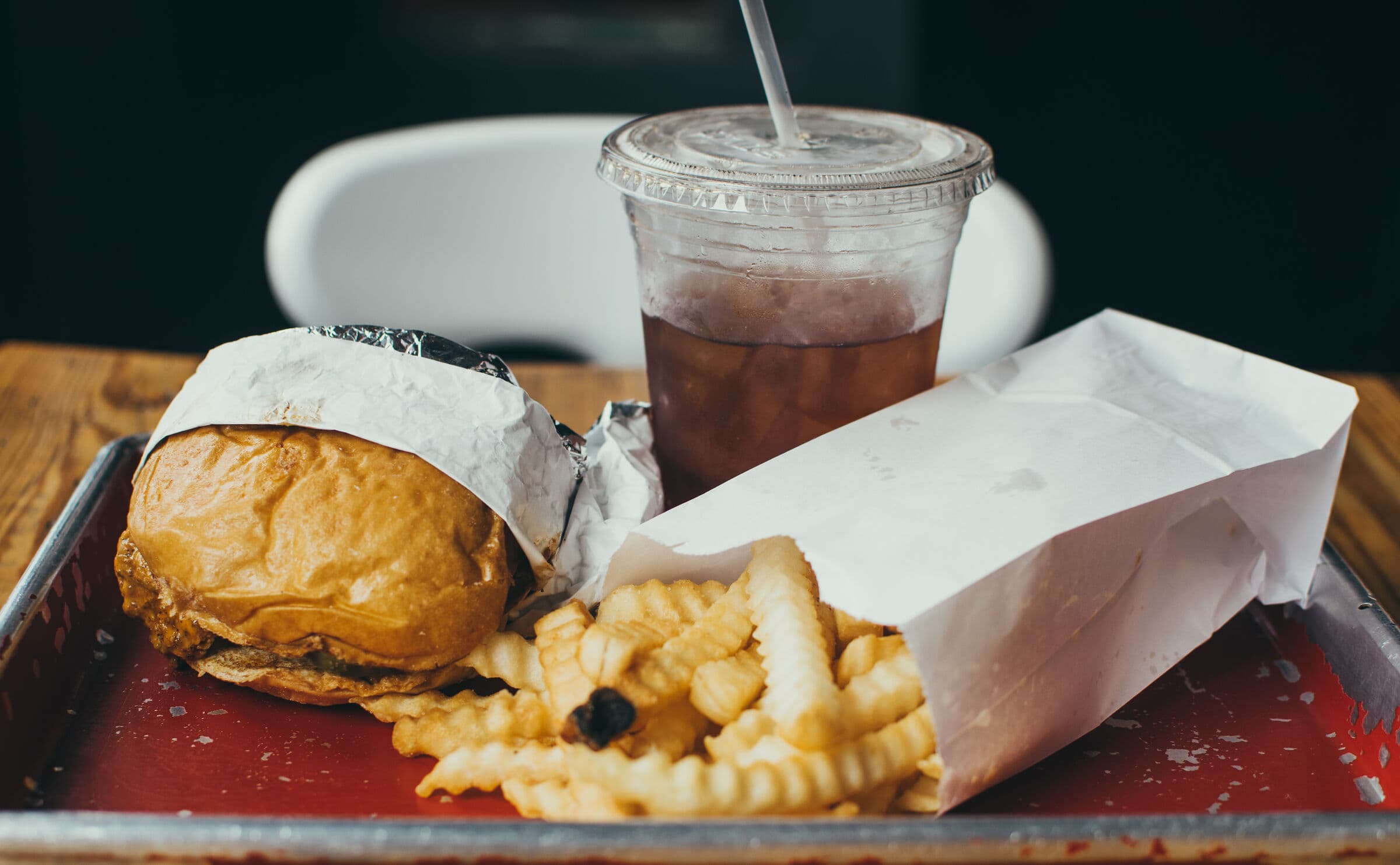 A fast food tray: wrapped burger, fries, and a soda