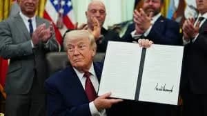 President Trump holding up a signed executive order in the Oval Office