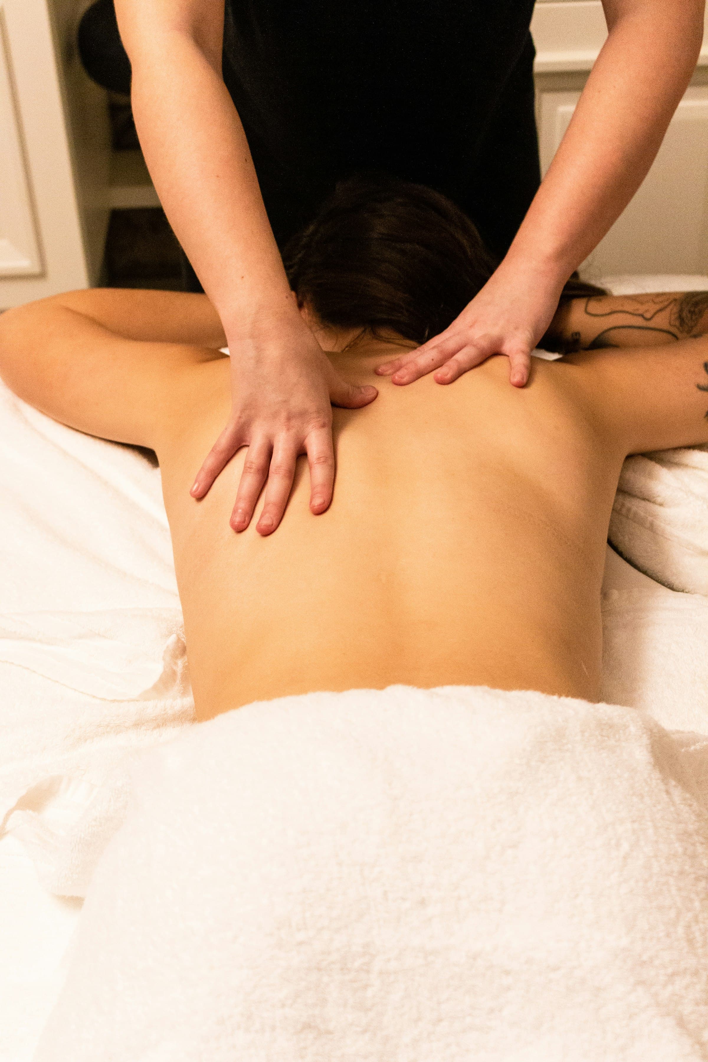 A massage therapist working on a client’s upper back at a spa table