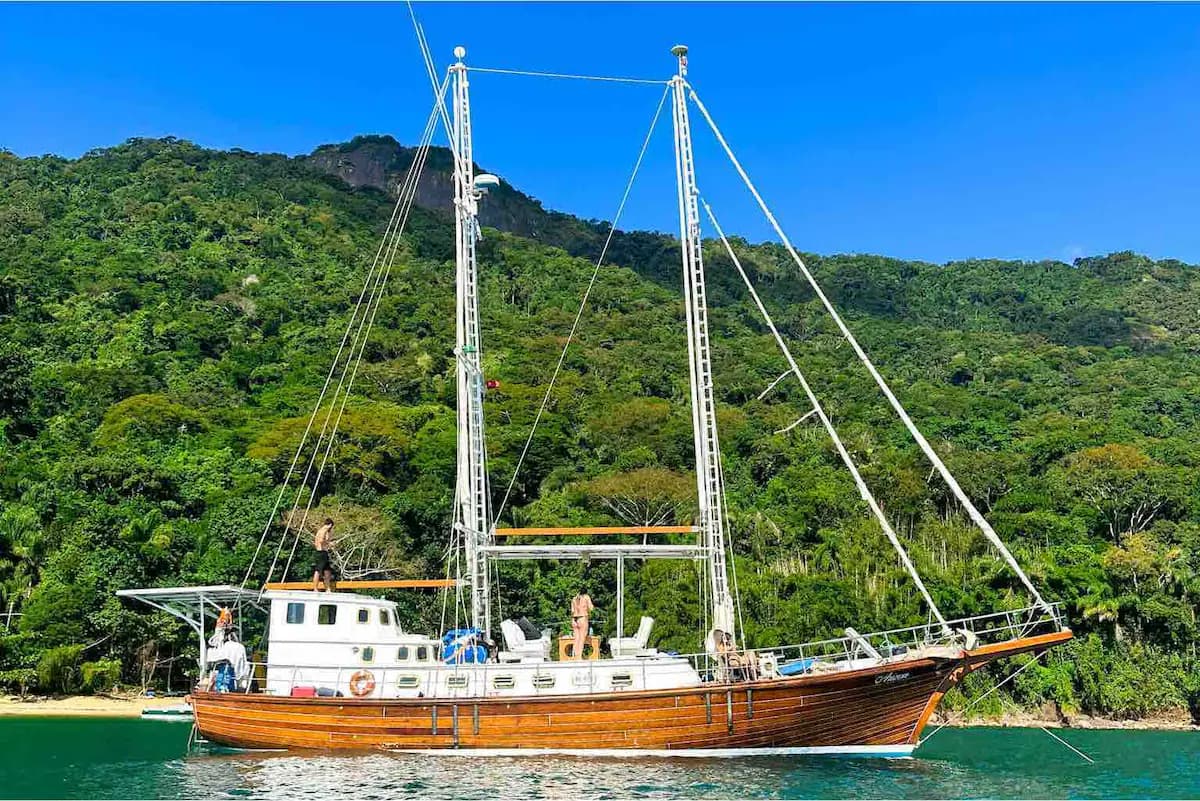 Velero de madera tradicional en la bahía esmeralda de Paraty con montañas selváticas detrás